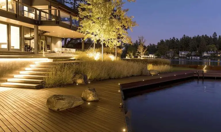 Waterfront deck with soft lighting and steps leading into a natural swimming area