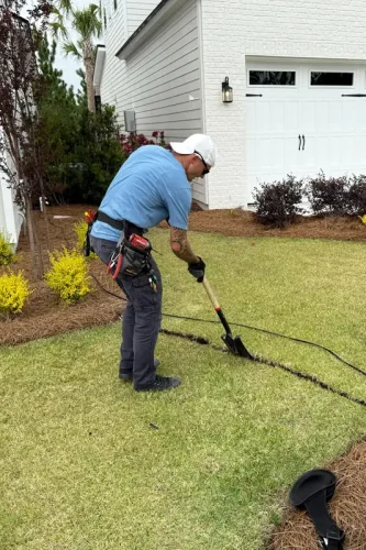 Technician trenching for path light wiring in residential front yard in Panama City