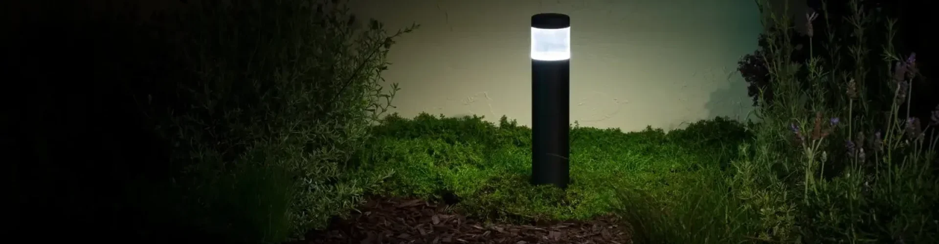 Modern black bollard-style garden light illuminating surrounding plants
