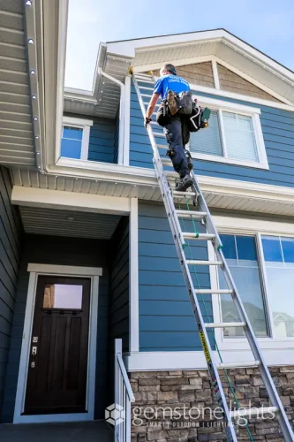 Installer climbing ladder to install soffit LED lights on house exterior