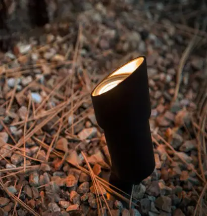 Close-up of outdoor landscape lighting fixture properly aimed and illuminated among pine needles and gravel