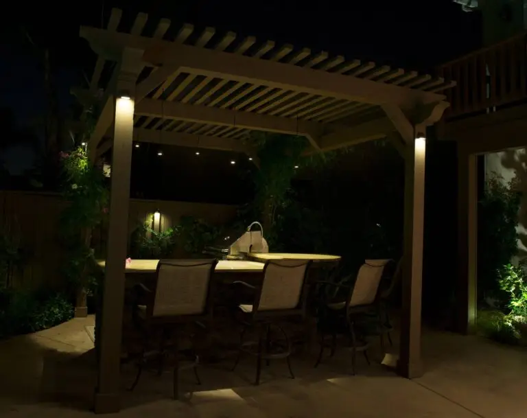 Pergola-covered outdoor kitchen with soft lighting and bar seating for family meals