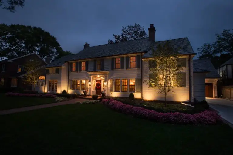 Warm architectural lighting highlights front elevation and trees of a classic colonial-style home