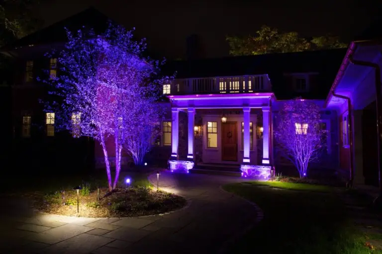 Purple LED landscape lights highlight trees and porch columns at night