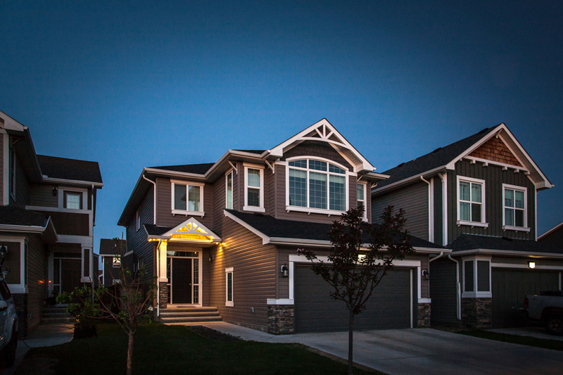 Two-story home at dusk with minimal warm porch lighting and no roofline lights - before.