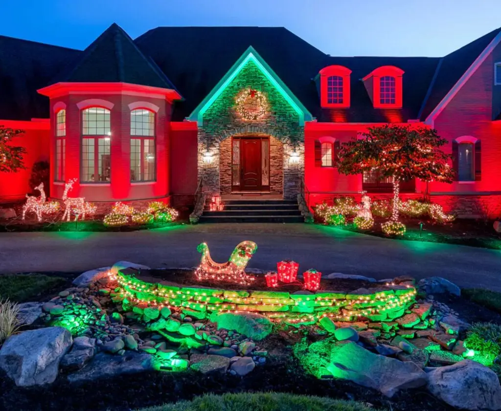 A home beautifully lit in festive red and green lighting with decorations and welcoming curb appeal.