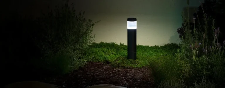 Modern black bollard-style garden light illuminating surrounding plants
