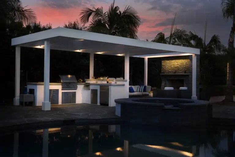 Contemporary outdoor kitchen and lounge with built-in lighting near poolside at sunset
