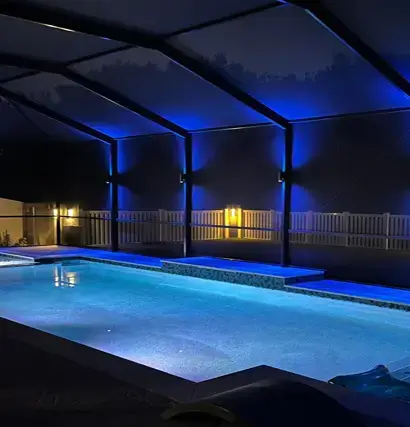 Covered backyard pool with blue LED lighting on the enclosure at night